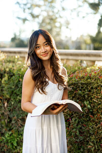 High school senior girl reading a book outdoors near greenery during Yucaipa senior portrait session by Kaitlyn Dawn Photography.