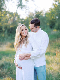 Husband hugging pregnant wife from behind and holding her pregnant belly in Magnuson Park