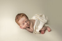 sleeping newborn wearing white outfit posed in heart