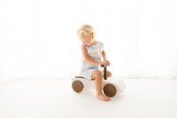 Toddler rides a wooden car Baby smiles at the camera during his Cake Smash Photoshoot at Holy City Babies Portrait Studio in Charleston, SC.