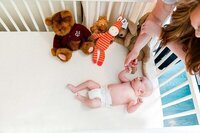 Newborn photography in a cozy nursery with a baby lying on a changing table, surrounded by plush toys.