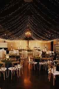 String lights and chandelier hanging over dance floor and wedding reception.
