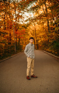 A New Berlin West High School student stands in the middle of a Delafield road lined with trees in full autumn color for his senior portraits.