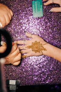 Applying a henna design on a hand over a sequined purple surface.