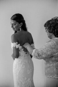 bride gets buttoned up by mom into her wedding dress
