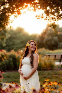 A pregnant mom cradles her belly in  a garden.