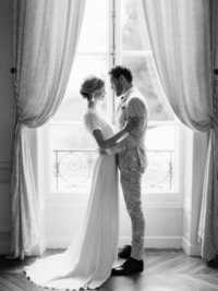 Young married couple embrace in front of window during anniversary photo session in French manor