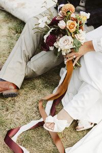 Close up of bride's bouqet while bride and groom sit on grass