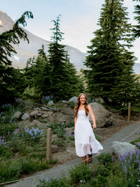 Sandy High School senior portraits at Timberline Lodge walking along the paths with summer wildflowers wearing a white dress.
