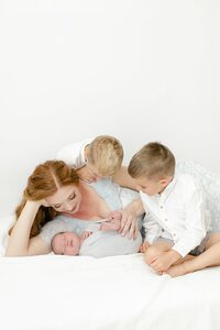 mom holding baby while two older brothers watch over
