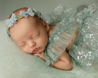 Newborn baby resting with hands under face on a soft green blanket. Photographed by Inland Empire newborn photographer Kaitlyn Dawn Photography.