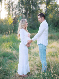 Couple standing facing each other, holding expectant mom's pregnant belly