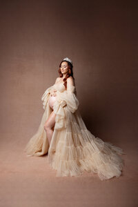 Pregnant woman posing in a dramatic champagne maternity gown with crown during a fine art studio maternity session by Kaitlyn Dawn Photography.