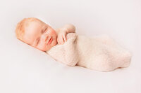 Newborn baby wrapped in cream fabric photographed by a New Bern newborn photographer