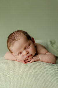 Sleeping newborn baby posed on a soft green backdrop during a studio newborn photography session with newborn photographer Kaitlyn Dawn Photography.