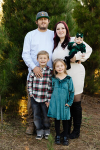 Outdoor family portrait in a natural green setting with parents and three children standing together in warm golden light, captured by Kaitlyn Dawn Photography, professional outdoor family photographer.