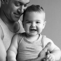studio portrait of father and  baby son father embracing him, baby is smiling and looking at camera