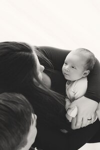 Army dad holding newborn baby close in soft neutral family portrait