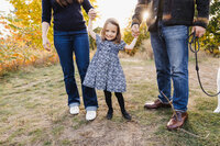 Little girl in floral blue dress being swung between her parents.