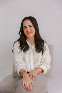 Woman sitting with a white linen top, giving a soft smile