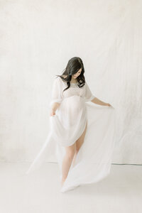 A photo taken for a maternity session in a Dallas/Fort Worth area photography studio of an expecting mother while she is dancing playfully around the studio.