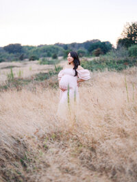 Pregnant asian woman standing in a grassy field at Discovery Park in Seattle