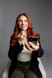 Professional woman with red hair applying lipstick while seated in studio. Photograph by Yucaipa branding photographer Kaitlyn Dawn Photography.