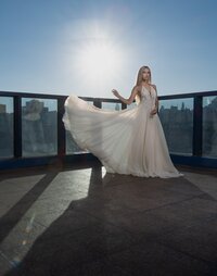 A woman in a flowing white gown stands on a rooftop terrace at sunset, city buildings behind her, sunlight streaming and casting long shadows—captured by a creative portrait photography Washington DC specialist.
