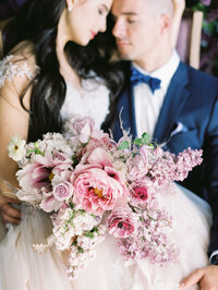 bride sitting on groom’s lap holding a lush bouquet with both eyes closed in a romantic portrait