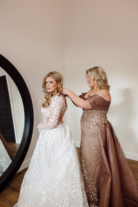 Husband and wife photographer capture mom putting on Bride's dress while getting ready for wedding