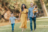 Family of four in mustard yellow and denim outfits walking hand in hand through a grassy park during a Cleveland family photography session