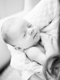 Black and white close-up of a sleeping newborn resting peacefully in mom’s arms during an in-home lifestyle session.