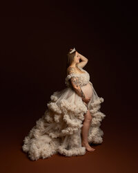 Pregnant woman in a flowing cream tulle maternity gown posing during a studio maternity photoshoot by Kaitlyn Dawn Photography.