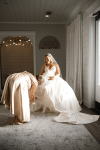 a mother of the bride adjusts the brides shoes in the bridal suite at chandelier farms