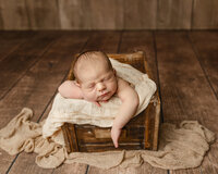 Sleeping newborn baby posed with arms resting over the edge of a wooden crate on a soft cream blanket during a classic studio newborn photography session photographed by Kaitlyn Dawn Photography.