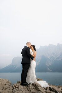 couple hugging on a rocky outcrop at lake minnwanka with the beautiful mt.inglismaldie in the background