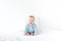 baby-sitting-on-bed-in-blue-sweater