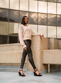 Senior girl in black leather pants and a cream sweater posing on a parking garage rooftop in downtown Mobile, Alabama.