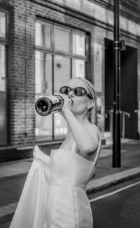 Bride in sunglasses drinking from champagne bottle