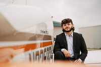 Senior portrait at a small hangar near Mobile International Airport in Mobile, Alabama — close-
up sitting on the wing with the plane reflecting beside him.