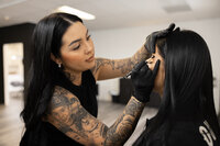 Tattooed woman concentrating while working on client’s brows in studio. Photograph by Yucaipa branding photographer Kaitlyn Dawn Photography.