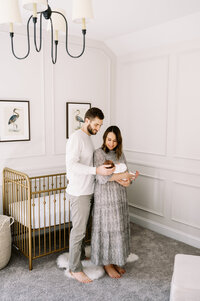 Couple holds newborn baby boy in front of gold crib in nursery