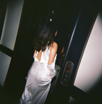 Flash film photo of a bride in a satin backless gown walking into an elevator during her New York City elopement.