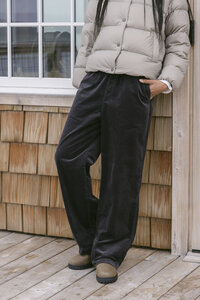 Cropped detail of black corduroy wide-leg trousers and suede boots against cedar shingle