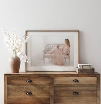 Framed studio portrait leaning on a wooden dresser alongside dried florals in a neutral home interior