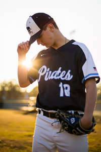 Teen boy baseball player tips his baseball cap as sun shines through