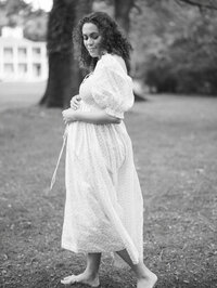 Black and white image of a woman softly smiling and caressing her pregnant belly in an outdoor maternity session in Seattle