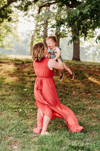 Mom swinging around with her one year old son.  Mom is wearing dusty rose dress from Baltic Born, and son is wearing sage romper from zara.  photo taken at Rockford Park by South Jersey family photographer, kristi