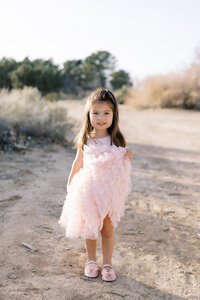 Young girl from the Parker family wearing a soft pink dress standing on a desert path in Las Vegas, smiling during a natural light family photography session.
