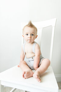 boy with mohawk sitting on chair and wearing suspenders